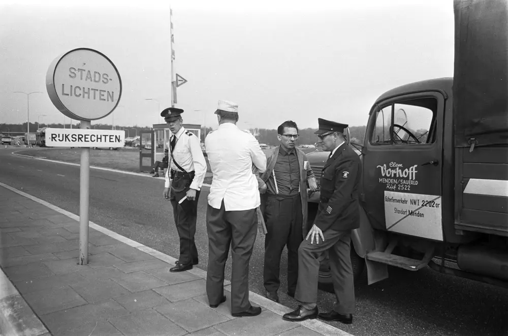 Customs officers and a driver talk beside a German truck at a border post with the sign Rijksrechten.