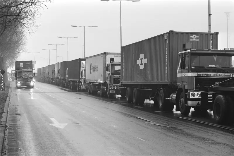 A long line of trucks with containers waits along a wet road in Rotterdam.